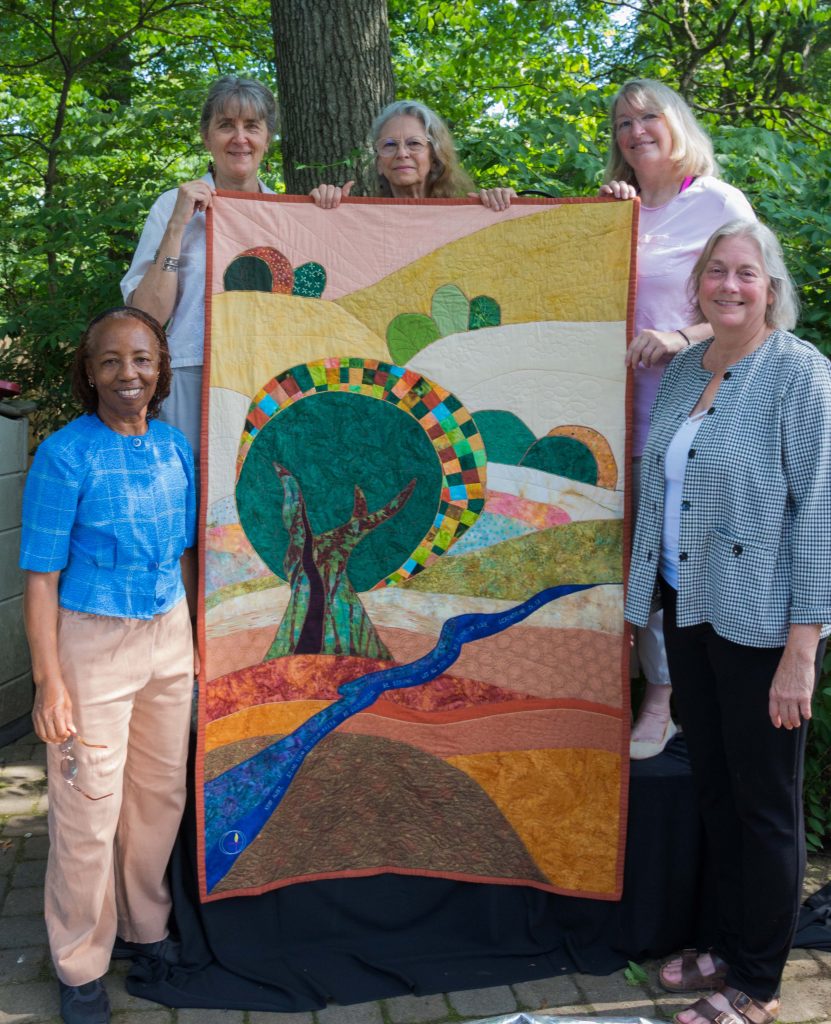 All five team members holding up the completed quilt