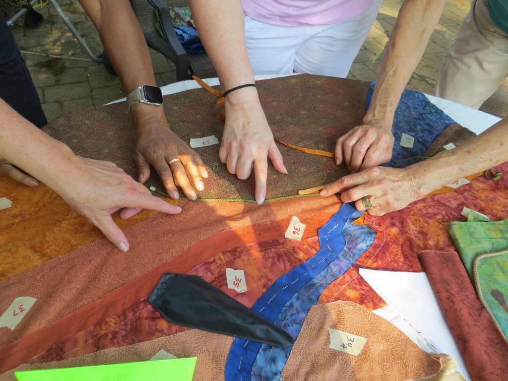 Hands of the team members pointing to and holding parts of the quilt fabric