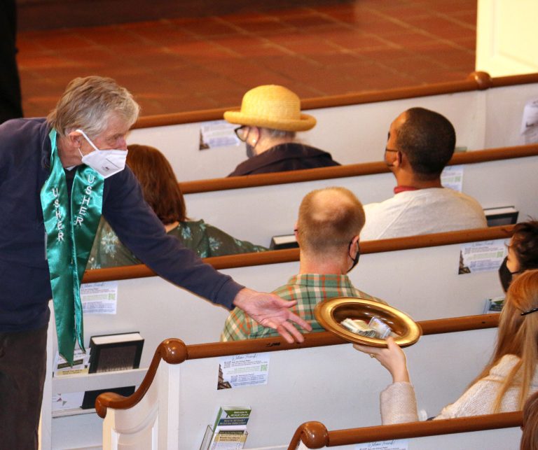 Photograph of an Usher passing the collection plate to a congregant during a Sunday service.