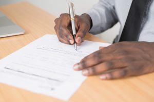 Picture of hands signing a document on a desk.